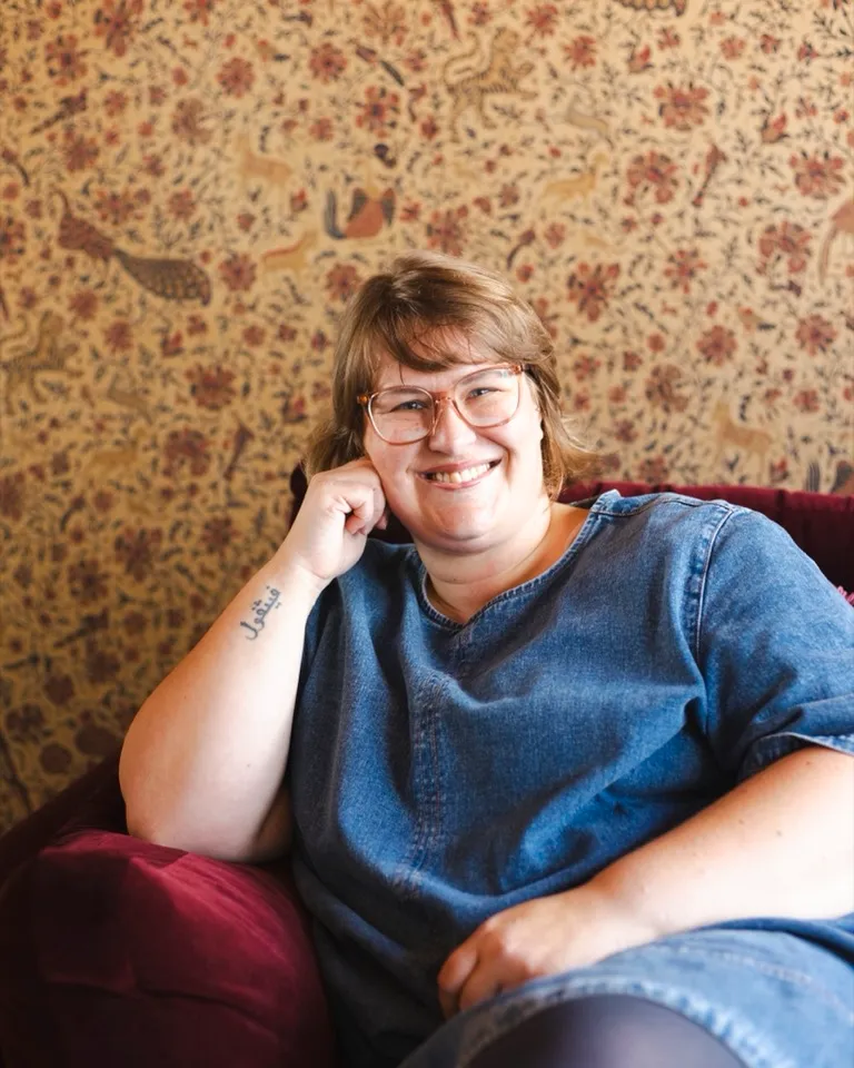 Gemma, founder of My Wedding Vibe, smiling in a chair against retro floral wallpaper