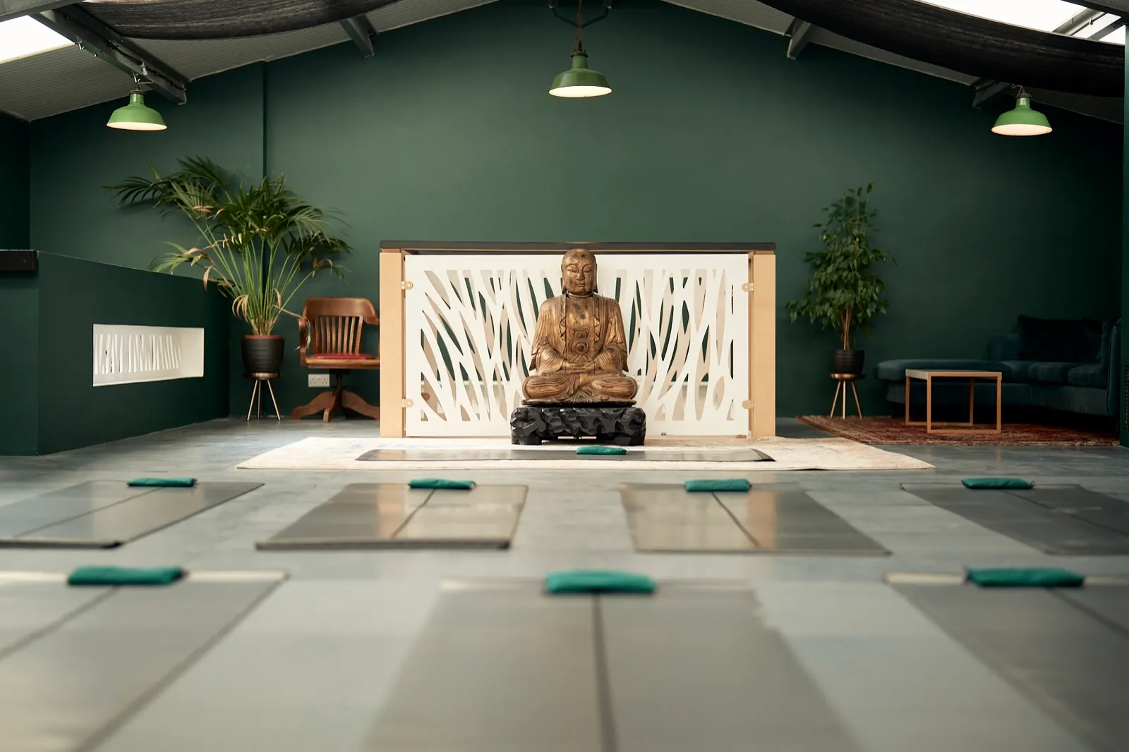 The studio at Woodsmoke in Wareham, deep green walls, mats laid out on the floor and a carved figure at the far end