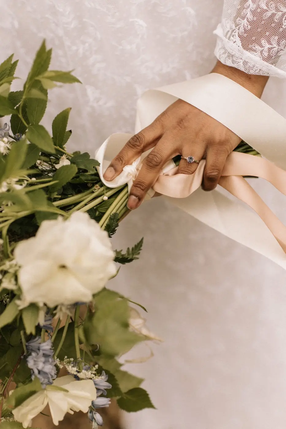 Hands in a lace sleeve holding the wild bridal bouquet, ribbon trailing